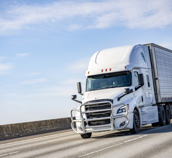 Commercial big rig white industrial long haul semi truck transporting frozen cargo in refrigerator semi trailer driving on the multiline interstate highway road with one way traffic direction